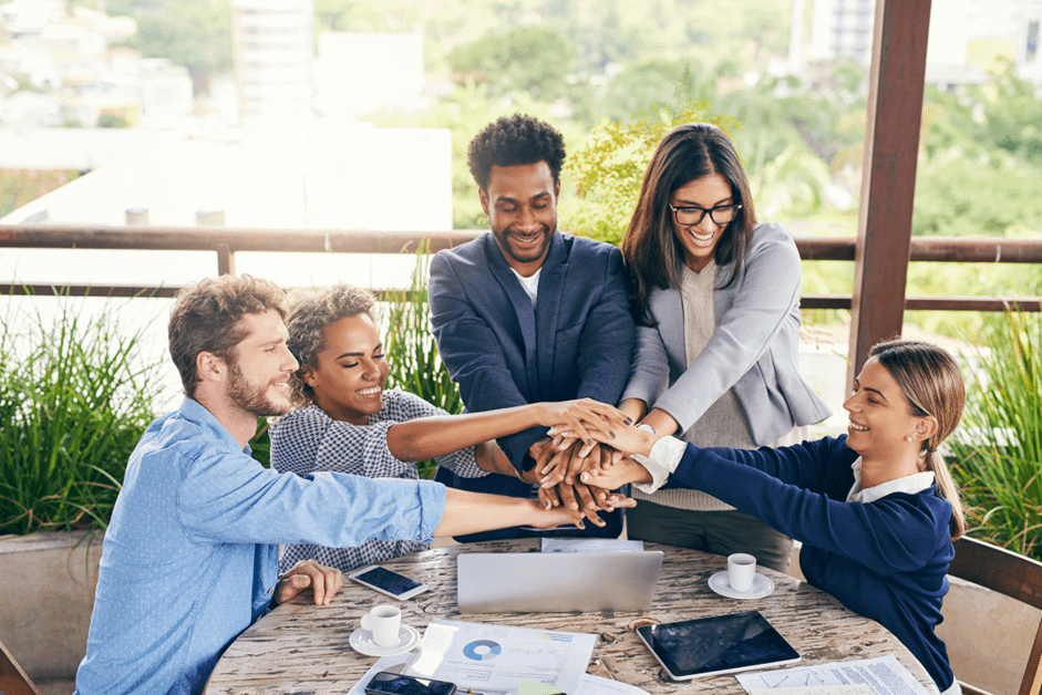 Smiling diverse group of employees high-fiving in a bright modern office, symbolizing teamwork and positive morale.